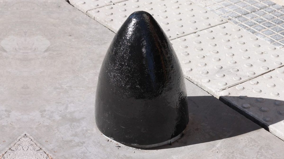 Bolardo Bala de fundición pintado de negro sobre una vereda con baldosas podotáctiles
