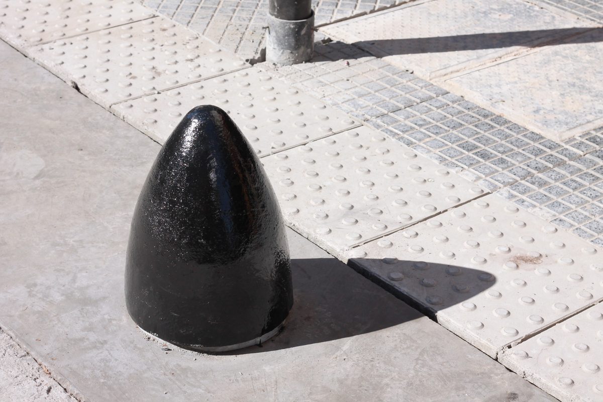 Bolardo Bala de fundición pintado de negro sobre una vereda con baldosas podotáctiles