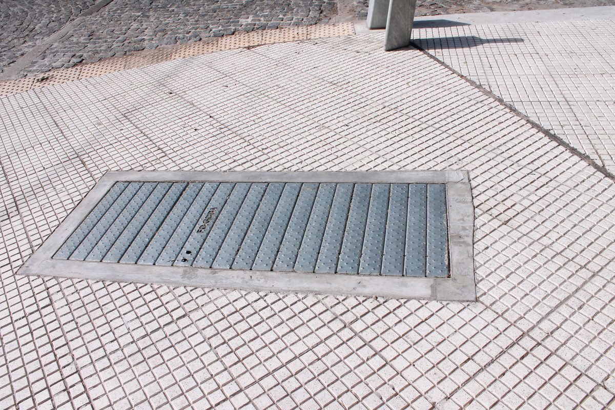 Tapa de cámara galvanizada instalada en una vereda con baldosas